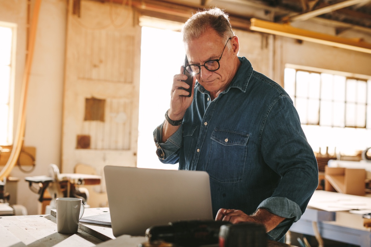 Senior male carpenter talking on phone and looking at laptop; representing "Best small business loans"