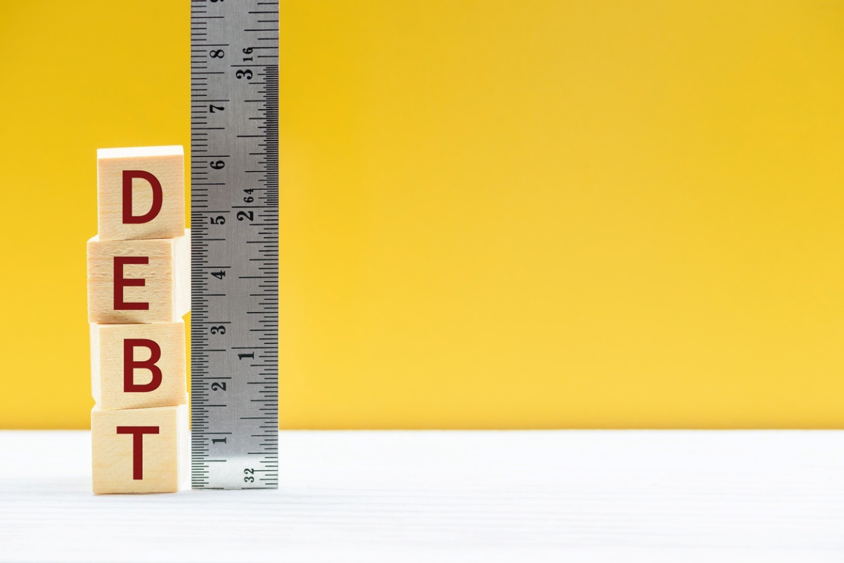 Vertical ruler with stacked wooden blocks spelling "debt" beside it, representing debt-to-income ratio