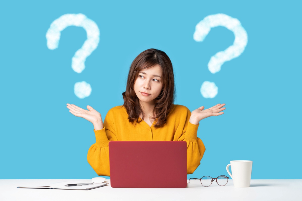 Young woman with questioning expression looking at a computer with a question mark over each shoulder, representing the differences between collateralized vs Non-collateralized loans